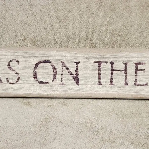 Partial rustic wooden sign with faded text on a textured wall.