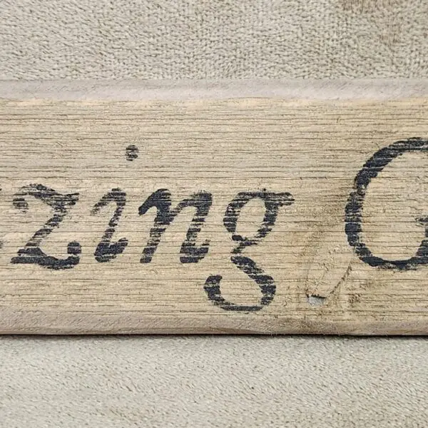 Partial wooden sign with faded cursive text on a textured wall.