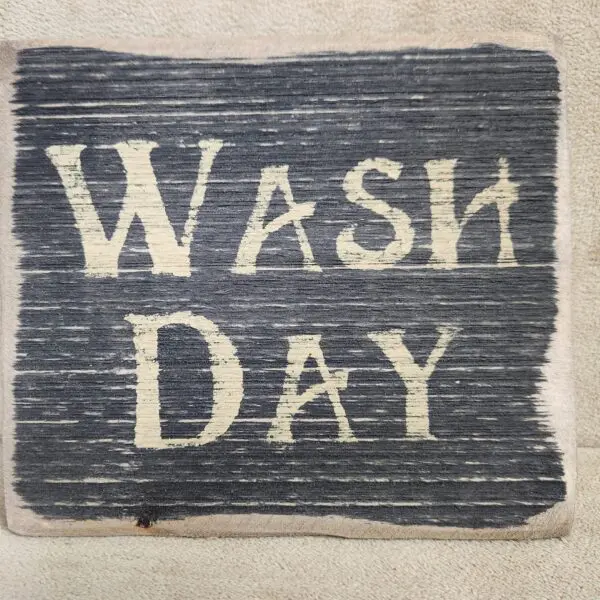 A rustic sign with the words 'WASH DAY' painted in white on a dark wooden background.