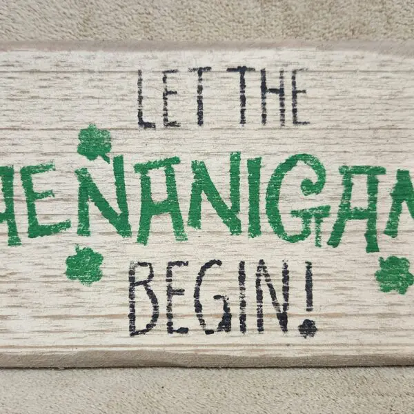 Rustic sign saying 'Let the shenanigans begin!' with green shamrocks.