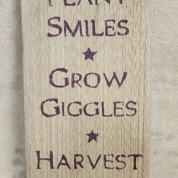 A rustic sign with positive words: Plant Smiles, Grow Giggles, Harvest Love.