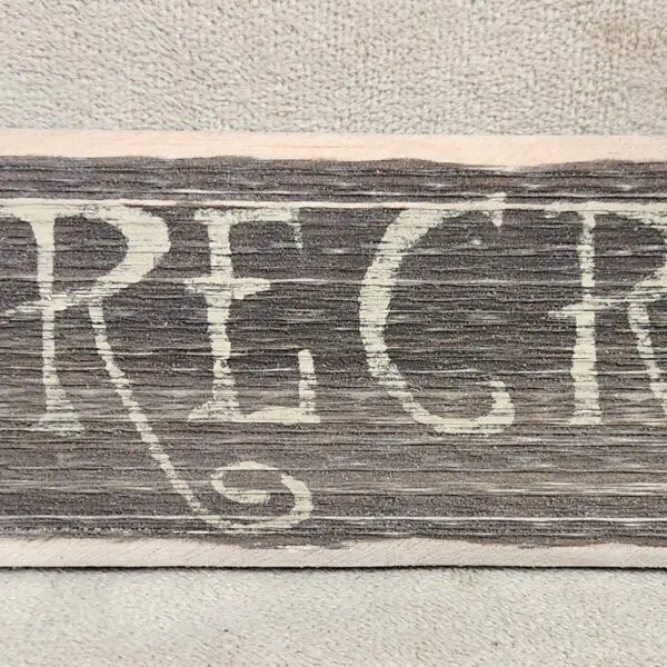 Rustic wooden sign with the word 'REGRET' painted in white.