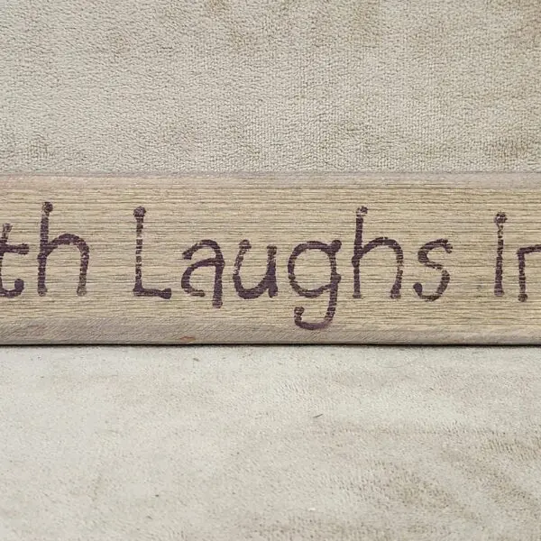 Wooden sign with the phrase 'Faith Laughs in the Face of Fear'.