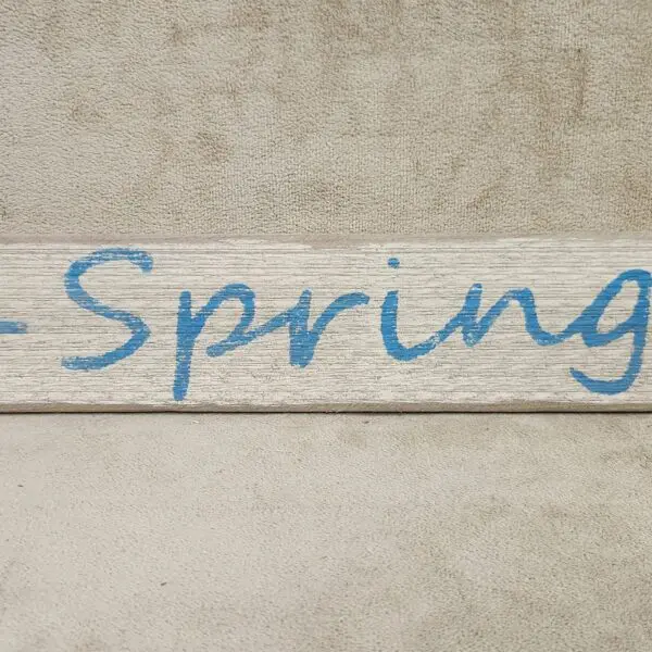 A wooden sign with the word 'Spring' painted in blue.