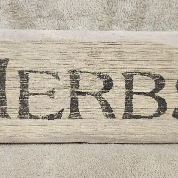 A wooden sign with the word 'HERBS' engraved on it.