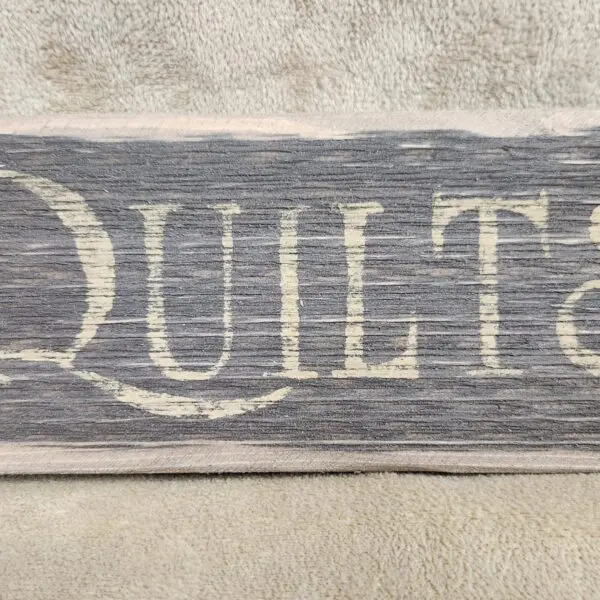 Rustic wooden sign with the word 'QUILTS' painted in white.