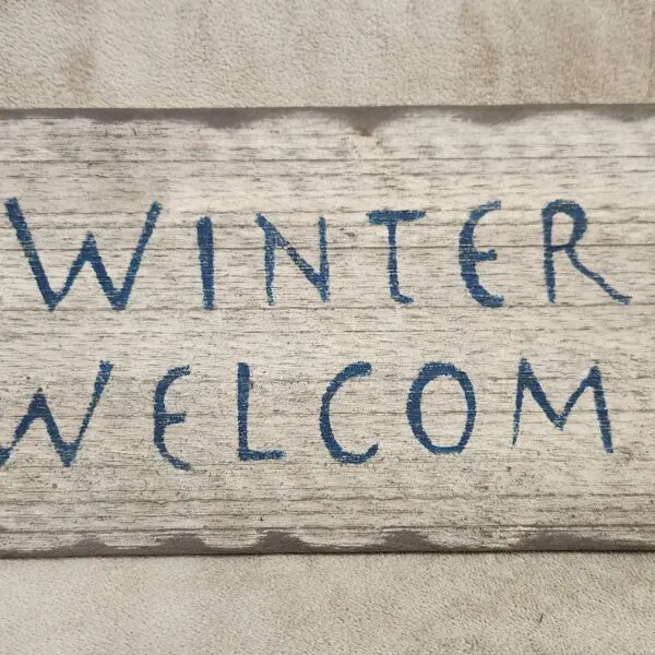 Hand-painted 'WINTER WELCOM' sign on a rough concrete surface.
