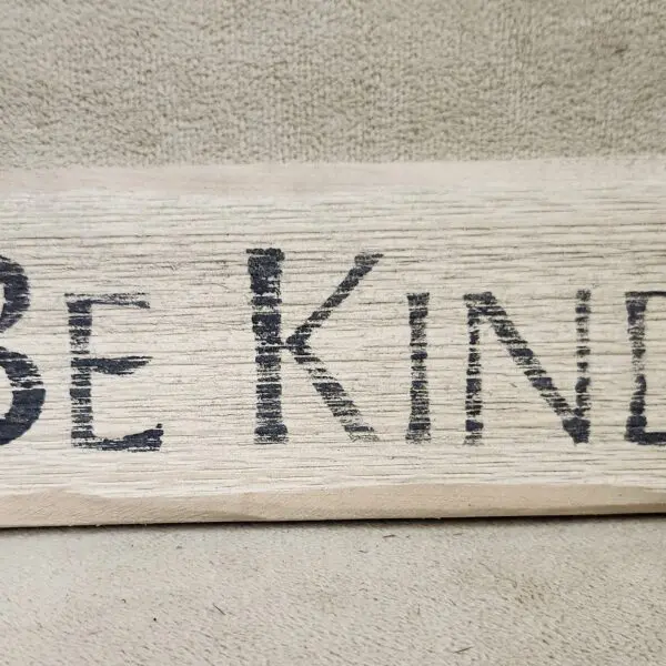 A wooden sign with the phrase 'Be Kind' written in black letters.